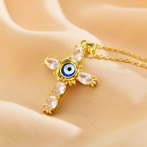 Macro shot of gold cross necklace with blue evil eye and clear crystals on silk