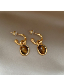 Close-up of gold-plated oval tiger eye earrings on a champagne silk fabric background