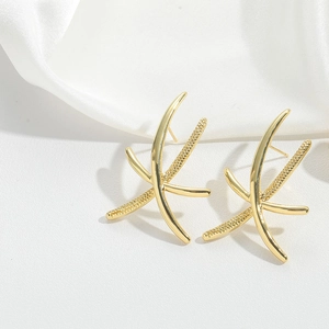 Macro shot of gold crisscross streamline earrings on elegant white silk background