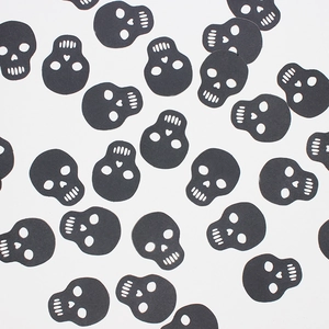 Halloween black skull confetti decorations scattered on white background for party decor