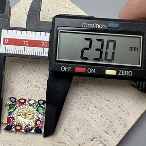 Macro shot measuring a square Virgin Mary pendant with colorful stones and gems using a caliper
