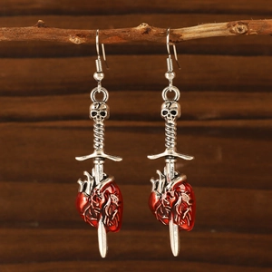 Gothic silver sword earrings with red heart and skull detail on a rustic wood background