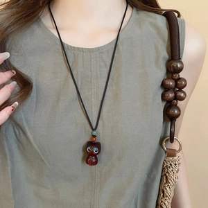 Close-up of a carved wood cat pendant necklace on a braided rope worn by a model