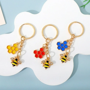 Three-piece gold bee and honeycomb keychains in yellow, red, and blue on a cloud stand