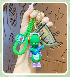 Close-up of a green cartoon dinosaur keychain with headphones and a guitar accessory