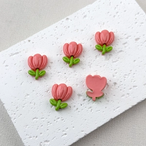 Detail shot of five pink resin tulip charms for DIY crafts on a textured white mat