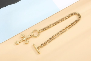 Macro detail of gold rose cross pendant and heart toggle clasp on layered bracelet