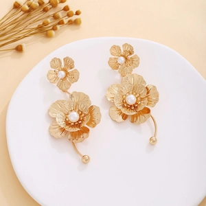 Macro shot of gold floral earrings featuring layered petals and central pearls on a tray
