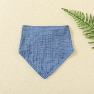 Blue double-layer muslin cotton baby bib with crinkle texture on warm neutral background