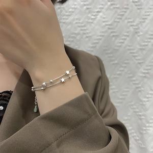 Detailed view of layered silver star bracelet on wrist featuring delicate beads and charms