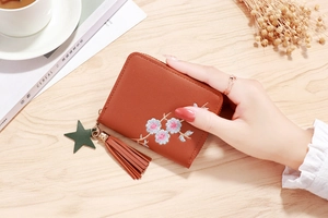 Detailed view of reddish-brown leather wallet featuring floral embroidery and star tassel