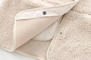Close-up of soft white teddy fleece texture with quilted lining and metal snap button