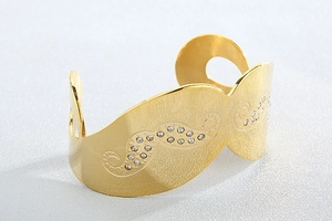 Close-up of golden wide cuff bracelet featuring brushed metal texture and wave rhinestone inlay