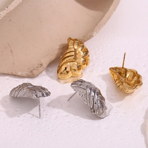 Detailed macro view of gold and silver fan-shaped textured earrings on stone with water drops