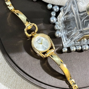 Detailed close-up of a horseshoe gold bangle watch featuring a white minimalist dial