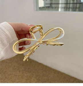 Macro detail of high-shine gold metal bow hair claw clip showing polished alloy texture