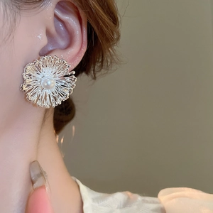 Elegant metal flower stud earrings with central pearl on model, minimalist fashion style