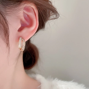 Detail of C-shaped gold earrings with white shell and zircon on a female model