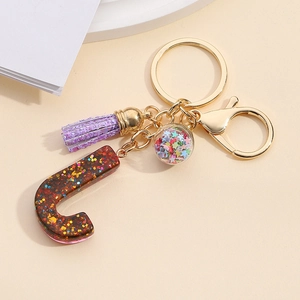 Detail of dark brown glitter resin letter C keychain with purple tassel and star sequins