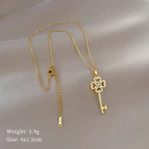 Gold titanium clover key necklace with sparkling stones on a soft silk background