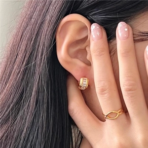 Close-up of minimalist gold huggie hoop earrings and a crisscross ring on a fashion model