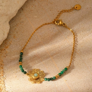 Detail of gold-plated bracelet with green beads and hollow floral pendant on stone