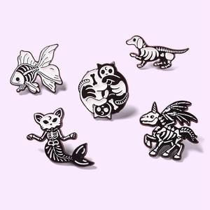 Detailansicht von fünf Emaille-Pins mit Skelettmotiven von Katze und Hund auf lila Grund