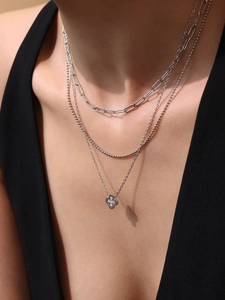 Detail of layered silver necklaces with a sparkling clover pendant on a model