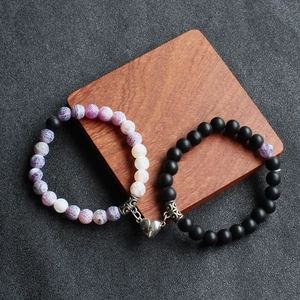 Detailed view of couple magnetic bracelets with purple stone and black matte beads on wood