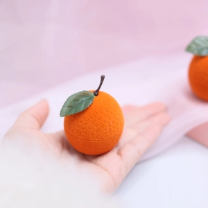 Close-up of cute orange-shaped jewelry box with soft velvet texture and green leaf detail