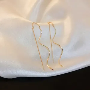 Minimalist gold wave tassel chain earrings with sleek long linear design on white silk