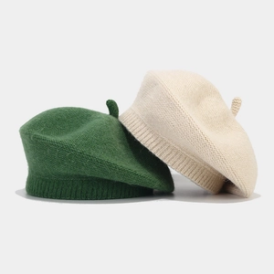 Detail of green and beige knitted wool berets showcasing fine texture and 3D design