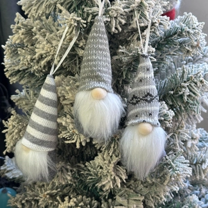 Three grey knitted Christmas gnomes hanging on snow-covered tree branches for festive decor