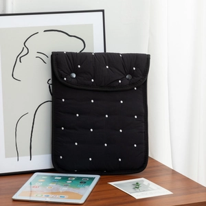 Detail of black quilted laptop sleeve with white polka dot embroidery and dual buttons