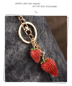 Detail view of gold keychain with vibrant red strawberry pendants on dark fabric