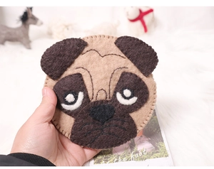 Close-up of a handmade pug-shaped wool felt pouch held in hand over a soft background