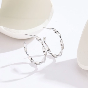 Minimalist silver Mobius twist C-shaped hoop earrings on white geometric stone