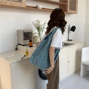 Blue canvas tote bag with white daisy floral pattern shown in a lifestyle shoulder view
