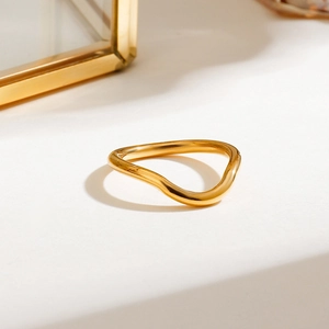 Close-up of elegant gold wave ring with high-polish metallic finish on a white surface