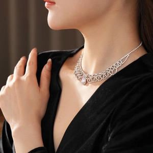 Close-up of a silver lace necklace with a pink teardrop gemstone on a model in black