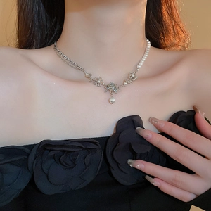 Detailed view of silver metallic rose pendant and white faux pearl necklace on model neck