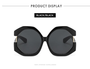Detailed close-up of oversized black geometric cat-eye sunglasses with gold metal accents