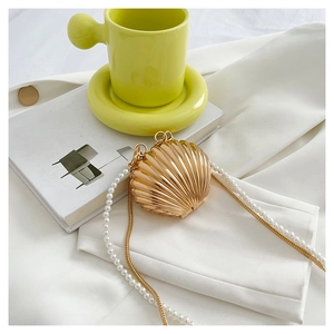 Detail of golden shell evening bag with pearl handle and metal chain on white cloth