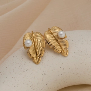Boucles d'oreilles feuilles dorées avec perles blanches sur présentoir en céramique