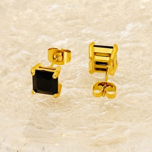 Macro shot of square black zircon earrings with gold plating on a water-textured base