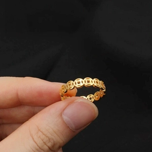Close-up of gold-colored ring featuring traditional Chinese coin patterns on black fabric