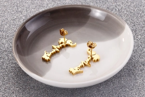 Macro detail of gold elephant heart-rate ear studs on a polished ceramic dish