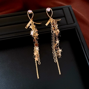 Detail of long gold chain tassel earrings with zircon stars on black leather tray