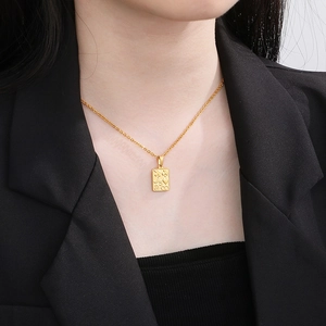 Close-up of golden rectangular charms engraved with celestial symbols on a fine chain