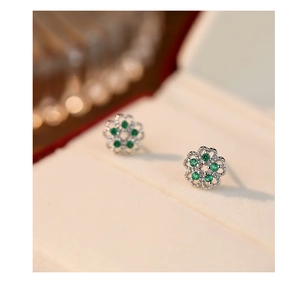 Macro view of sterling silver flower earrings featuring emerald green gemstone accents
